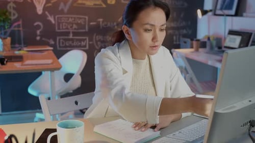 Female Entrepreneur Working in Dark Office Writing and Looking at Motinor Searching Information