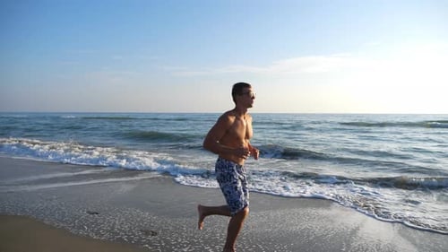 Athletic Handsome Guy Jogging Through Coast with Beautiful Seascape at Background. Young Sporty Man