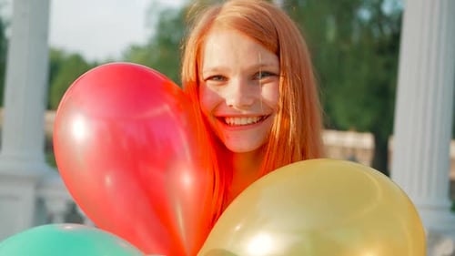Smiling Woman with Red Hair Holding Colorful Balloons