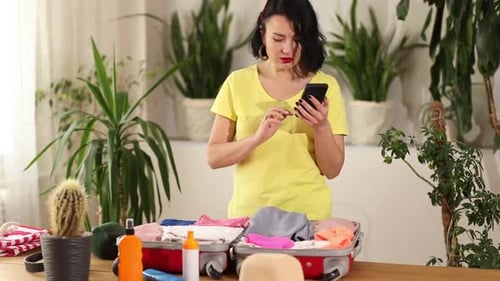 Woman Packing Suitcase While Using Smartphone