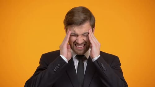 Stressed Man Massaging Temples Against Orange Background