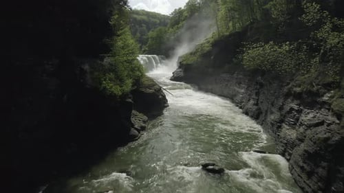 Drone shot, flying through a canyon, revealing a beautiful waterfall.