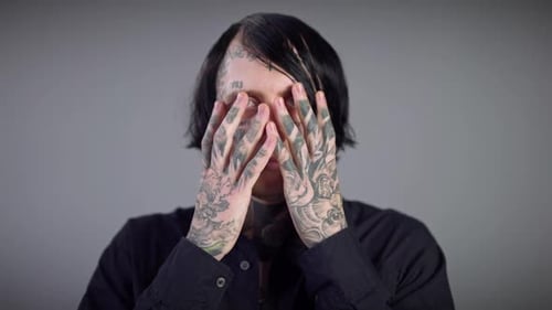 Tattooed man reveals face with hands