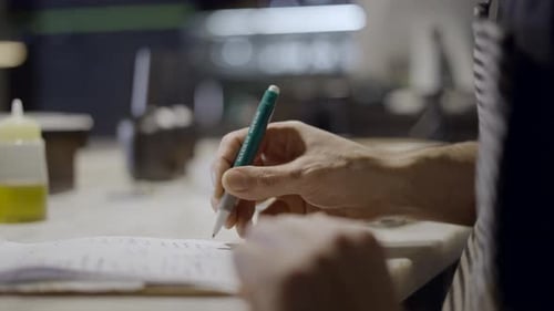 Side Closeup of Male Hand Writing on Notepad at Restaurant Counter