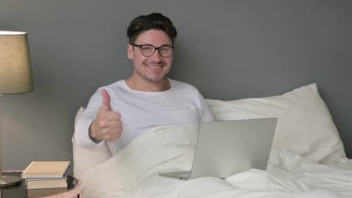 Signe du pouce levé par un homme d'âge moyen avec un ordinateur portable au lit