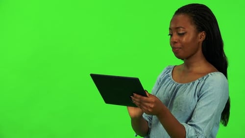 A Young Black Woman Works on a Tablet with a Smile - Green Screen Studio