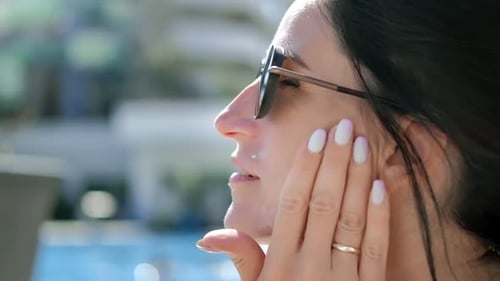 Closeup Face of Smiling Relaxed Woman in Sunglasses Applying Sunscreen Skin Cream During Sunbathing