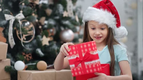 Excited Girl Opening Christmas Gift by Tree