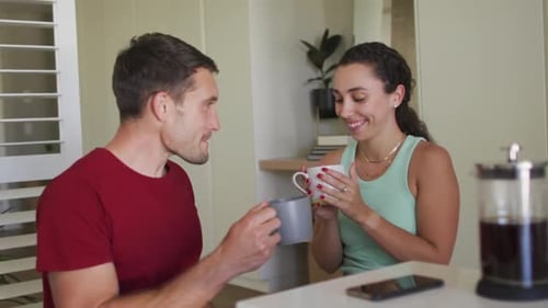 Happy caucasian couple drinking coffee and using smartphone
