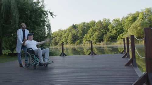 Doctor Walks with His Old Patient in the Park Near Lake
