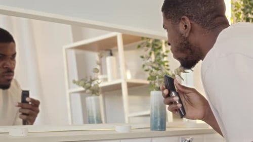 Man Trimming Beard With Electric Trimmer In Bathroom
