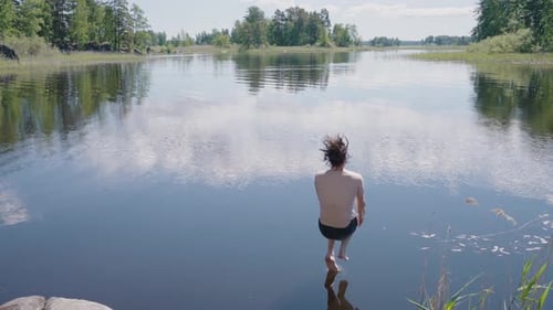 Junger Mann springt an sonnigem Tag vom Felsen in klares Seewasser