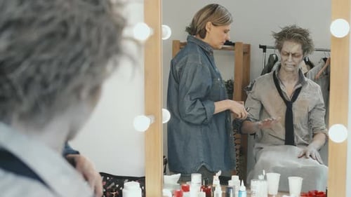 Artista de efectos visuales aplicando pintura corporal a un hombre con maquillaje de zombi