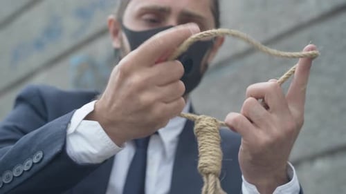 Nahaufnahme eines selbstmörderischen Seils in männlichen kaukasischen Händen mit verschwommenem verzweifeltem Mann im Hintergrund