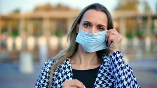 Woman Putting on Medical Mask Posing at City Park Fountain