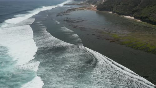 Aerial drone view of waves and surf breaking against a rocky reef at low tide