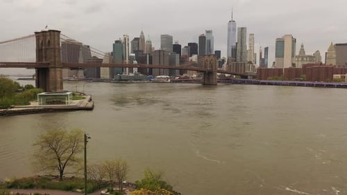 An aerial view over the East River on a cloudy day. The drone camera dolly out from the Brooklyn Bri