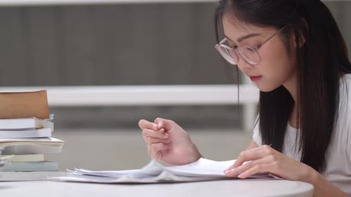 Student with Glasses Studies Textbook at Table
