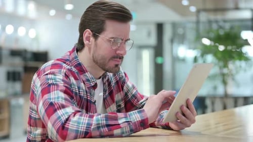 Man Frustrated While Using Tablet Indoors