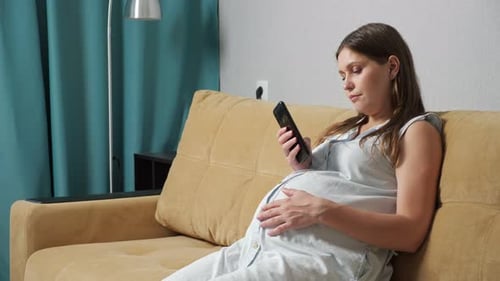 Pregnant Woman Relaxing on Couch Using Mobile Phone