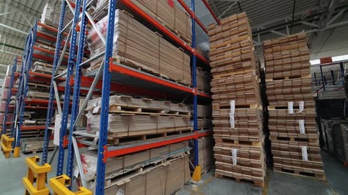 High metal shelves of blue color are filled with wooden boards in the building of a warehouse