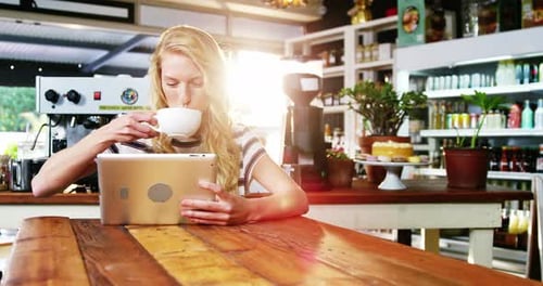 Woman Using Tablet and Drinking Coffee in Cafe