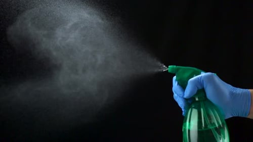 Gloved Hand Sprays Sanitizer Against Black Background