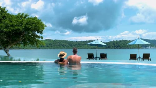 Couple European Man and Asian Woman in Infinity Pool in Thailand Looking Out Over the Ocean Luxury