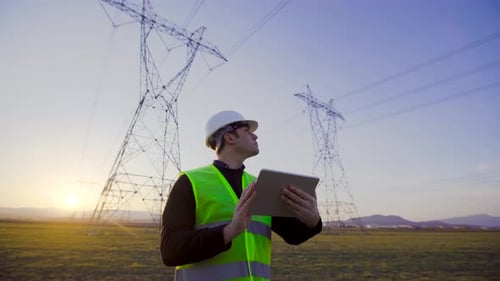 Ingenieur, der bei Sonnenuntergang vor Stromleitungen arbeitet.