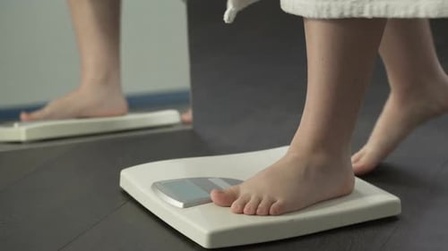 Weight problems, lady stepping on scales at home to check weight, extra fat