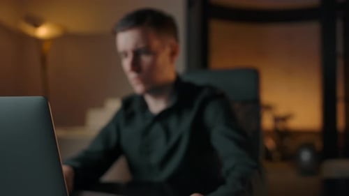 Man Working on Laptop in Dark Home Office