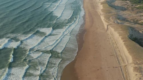 Few People on Wide Brown Beach Keeping Distance at Beautiful Golden Hour with White Green Waves