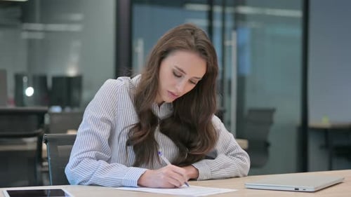 Beautiful Young Businesswoman Writing on Paper in Office
