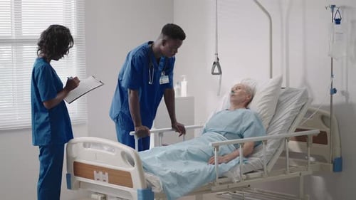 Senior Patient on Bed Talking to 2 African American Doctor in Hospital Room Health Care and