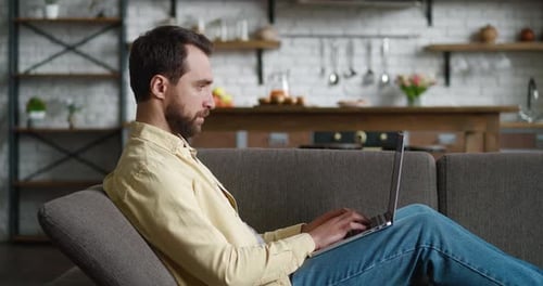 Man Relaxing on Sofa Typing on Laptop