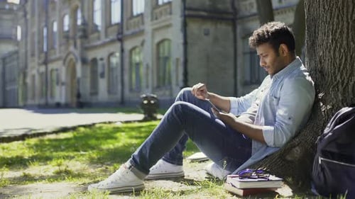 Male Sitting Under Tree, Using Mobile Phone, Reacting to Newsfeed, Confusion