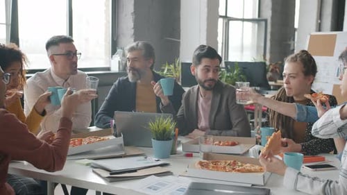Businesspeople Enjoyng Lunch Break at Work Eating Pizza and Drinking Talking in Office