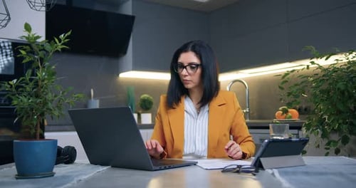 Empresaria sentada frente a una computadora en una cocina moderna y trabajando con documentos financieros