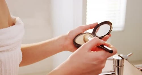 Woman Applies Makeup with Brush in Bright Bathroom