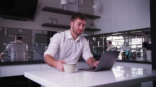young man works at a laptop and drinks coffee