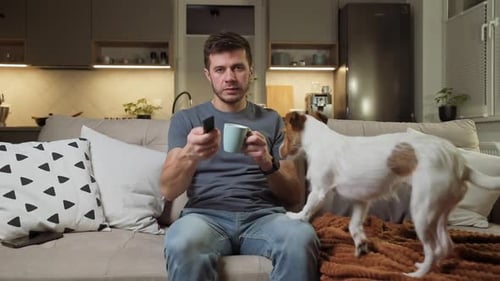 Man with Dog on Couch with Mug and Remote