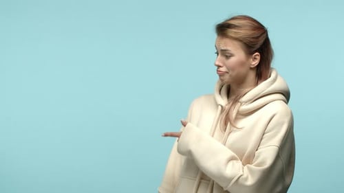 Привлекательная кавказская девушка в толстовке, одобряя кивает пальцем влево и показывает большой палец вверх