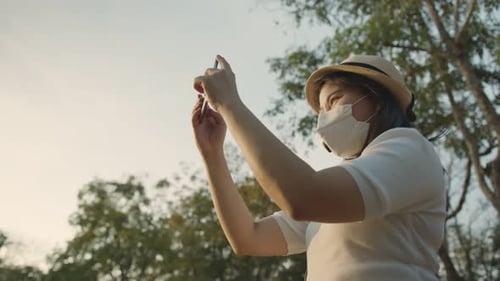 Woman Takes Photos with Phone in Park with Mask