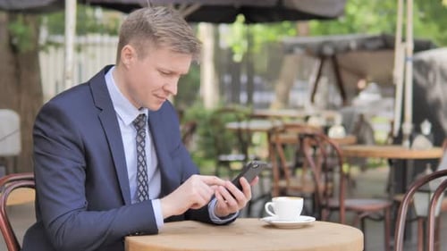 Businessman Upset By Loss on Smartphone Sitting in Outdoor Cafe