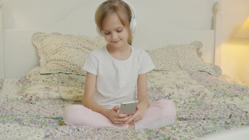 Girl with Headphones Using Phone on Bed
