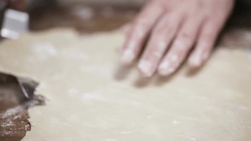 Person Flattens Dough on Wooden Table