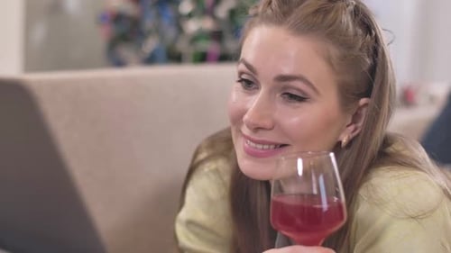Close-up Portrait of Happy Young Caucasian Woman Surfing Internet on Laptop and Drinking Red Wine