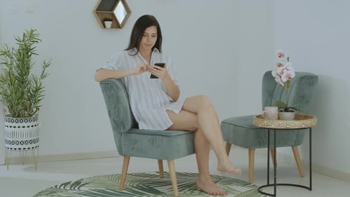Attractive brunette woman in casual clothes typing message on phone at home office