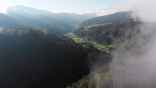 Flug durch die Wolken über das Karpatental mit Dorf im Sommer