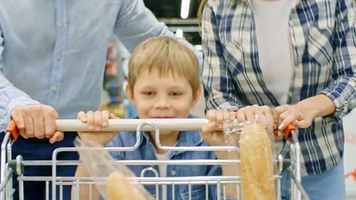 Boy Pushing Shopping Cart and Running with Parents in Supermarket